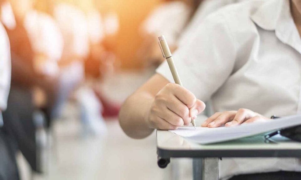 student writing at desk with pen