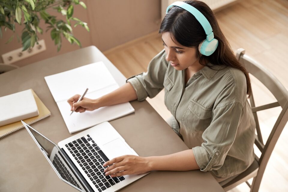 girl in headphones using laptop and holding pen