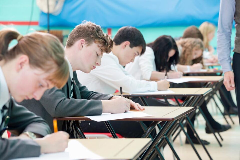 students in row of desks sitting paper exam